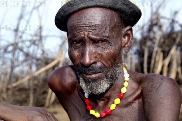 Elderly man with traditional collar sitting in a Dessanech village, Omorate, Ethiopia