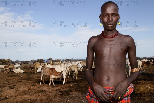 Man stands proudly in front of a herd of cattle in a Dessanech village, Omorate, Ethiopia