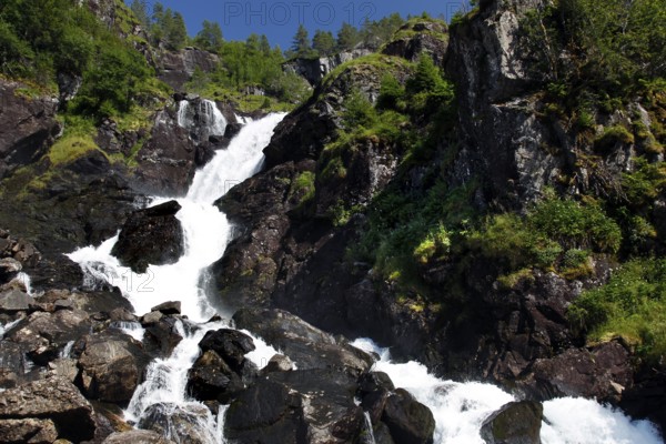 The impressive Låtefossen waterfall amidst rocky landscape and lush greenery, zero