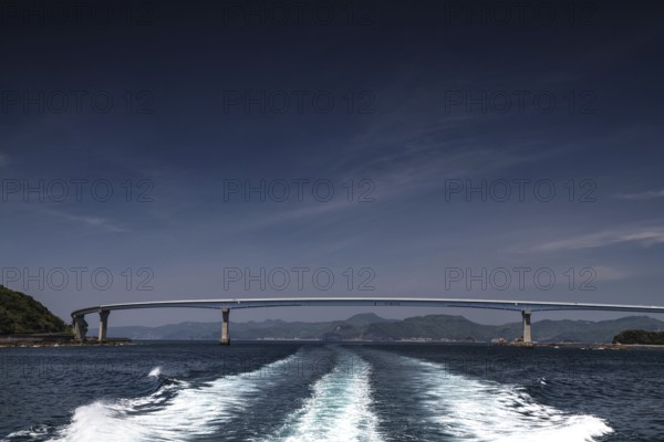 Bridge spanning the sea, with wave patterns in the foreground under clear sky, Nagasaki, Nagasaki, Japan