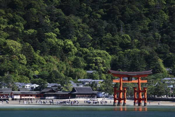 Torii of Itsukushima Shrine surrounded by trees as seen from ferry, Miyajima, Japan