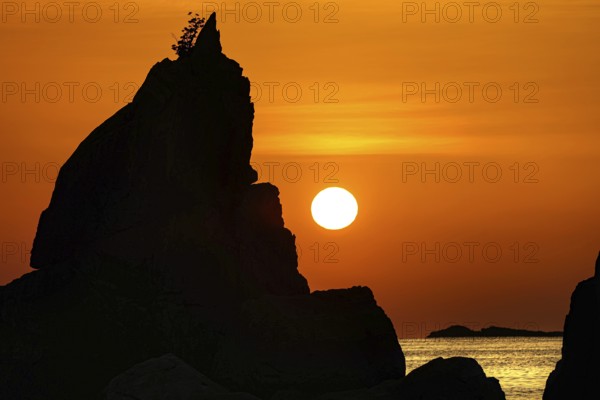 Single tall rock formation in glowing sunrise on the coast, Kushimoto, Japan