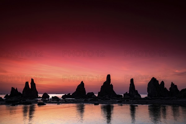 Dramatic rock formations in front of a bright, reddish sunrise, Kushimoto, Japan