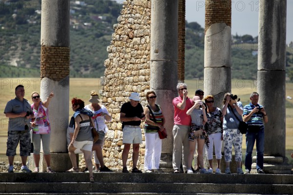 Tourists explore the ancient ruins of the Capitol in Volubilis in front of massive stone pillars, Volubilis, Fès-Meknès, Morocco
