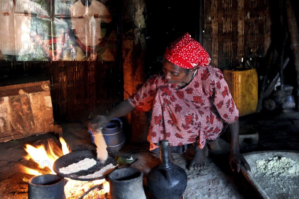 Woman wearing red clothes bakes traditional food in a hut over an open fire, Yirga Alem, Ethiopia