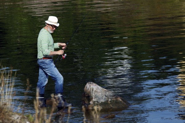 Angler with hat standing in water at a calm lake, Suomenlinna, Helsinki, Finland
