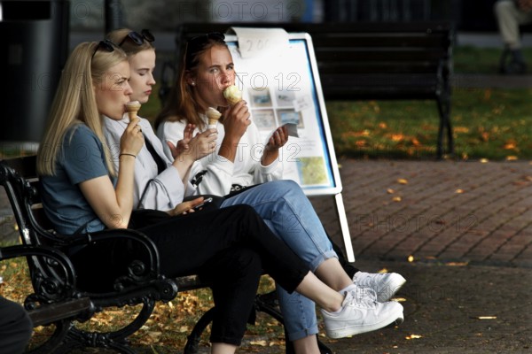 Women enjoying ice cream on a bench in autumnal Naantali, Naantali, Finland