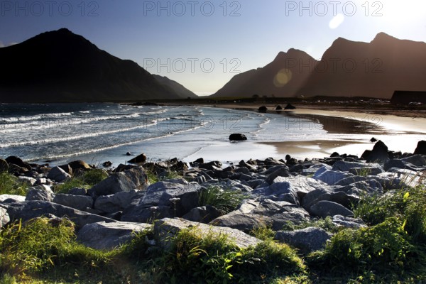 Sunny beach with views of mountains and calm waves surrounded by picturesque rocks, Flakstad, Lofoten, Norway