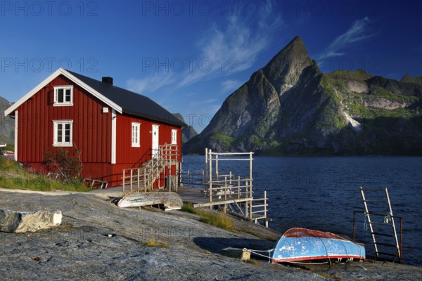 Red rorbu on the water with mountain panorama on Moskenesøy, Sakrisøy, Moskenesøy, Lofoten