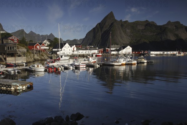 Sakrisøy harbour, where boats lie in calm water against a majestic mountain backdrop, Sakrisøy, Moskenesøy, Norway