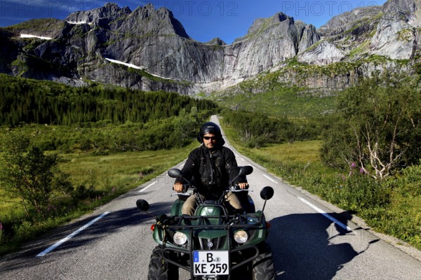 Man riding ATV on road in the mountainous landscape of Flakstadøy, Nusfjord, Flakstadøy, Norway