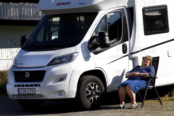 Female camper relaxing next to a white motorhome under a blue sky, Moskenesøy, Lofoten, Norway