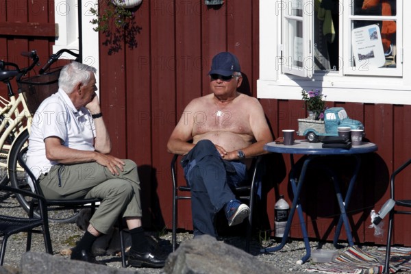 Two men relax in front of a café in the sun on the island of Å, Moskenesøy, Lofoten, Norway