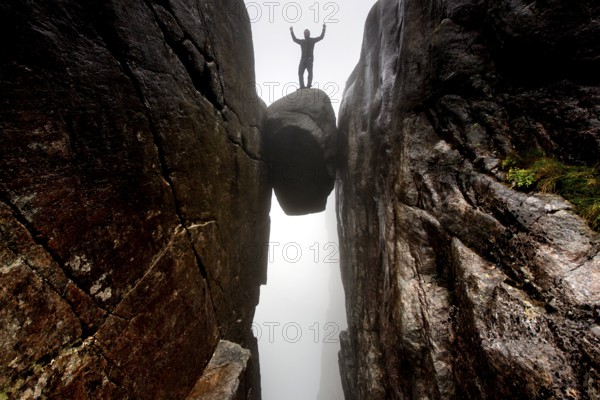Man standing triumphant on the famous Kjeragbolten Rock, Lysefjord, Rogaland, Norway