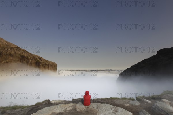 Person sitting and enjoying the misty view of Kjeragbolten, Lysefjord, Rogaland, Norway