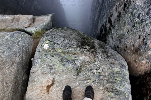 Two feet stand on a rock looking into the depths of Kjeragbolten, Lysefjord, Rogaland, Norway