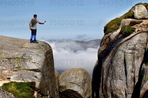 Tourist taking a selfie on cliffs near Kjeragbolten with clouds in the background, Lysefjord, Rogaland, Norway