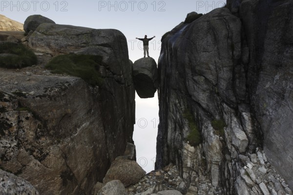 Adventurous person balancing on floating Kjeragbolten, Lysefjord, Rogaland, Norway