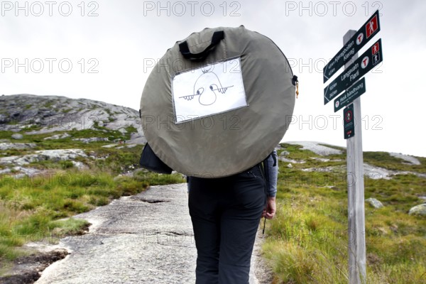 Hiker with tent in front of a signpost climbing Kjerag near Lysefjord, Kjerag, Rogaland, Norway
