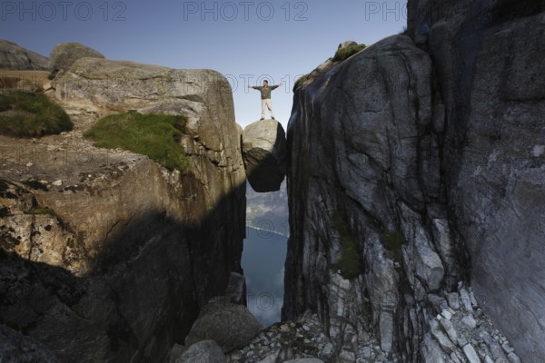 Individual posing on floating rock with arms spread out, Lysefjord, Rogaland, Norway