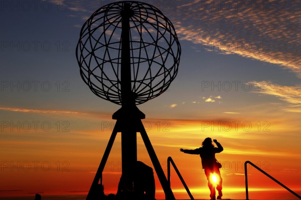 Person jumping on the North Cape globe in front of a breathtaking sunset, North Cape, Magerøya, Norway