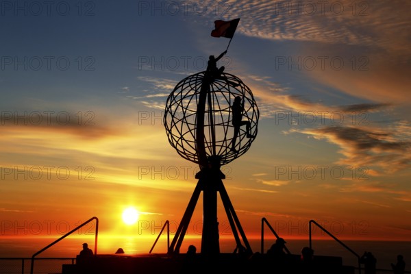 Man on the North Cape globe with flag at spectacular sunset, North Cape, Magerøya, Norway