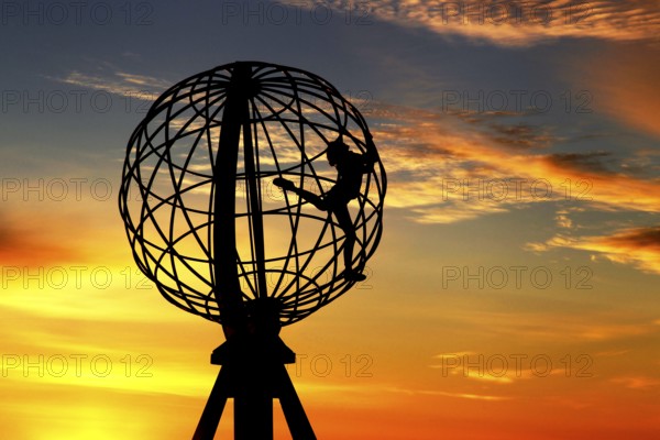 Silhouette of a climber on the North Cape globe in front of a colorful sunset, North Cape, Magerøya, Norway