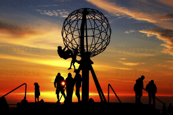Silhouettes of people on the North Cape globe in front of a glowing sunset, North Cape, Magerøya, Norway