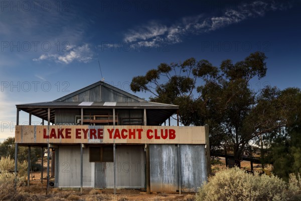 Dilapidated Lake Eyre Yacht Club building with eye-catching sign and trees, Marree, South Australia, Australia