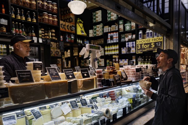 Sales stand with diverse delicacies and interacting customers at Queen Victoria Market, Melbourne, Victoria, Australia