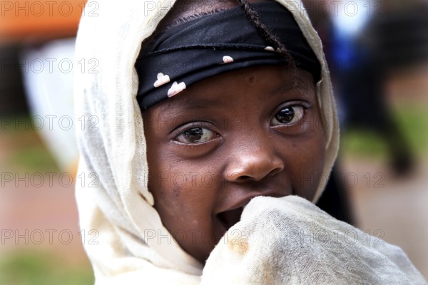 A child looks curiously at the camera, wrapped in a traditional headscarf, Key Afar, Basketo, Ethiopia