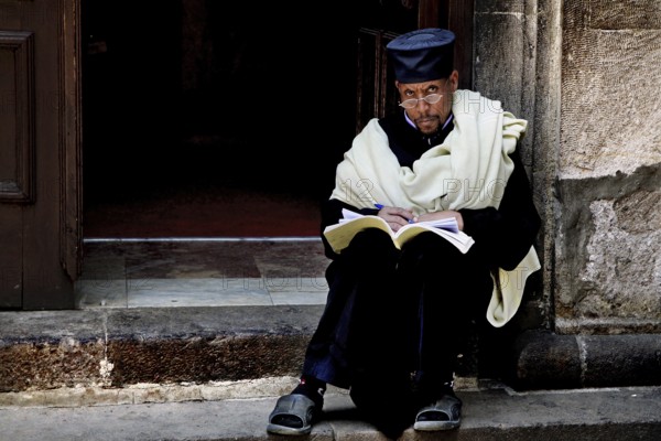 A priest sits reading on the steps of the Trinity Church in Addis Ababa, Addis Ababa, Ethiopia