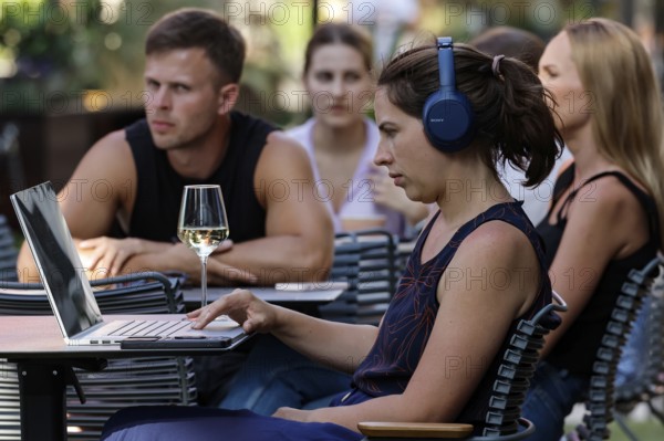 People relax in an outdoor cafe. A woman with laptop wearing headphones, Tallinn, Harju, Estonia