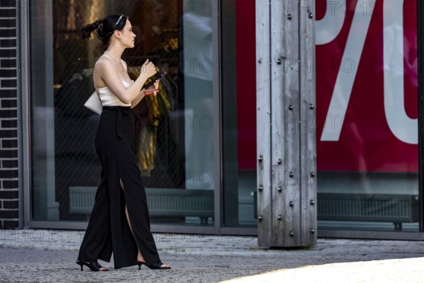 Woman walks by a shop while holding a cellphone and strolling through the neighborhood, Tallinn, Harju, Estonia