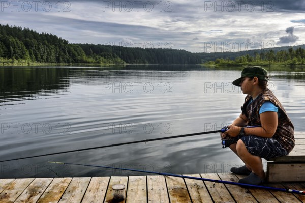 Young fisherman on a jetty on peaceful Ilgis Lake, surrounded by forest in Iginalina, Ignalina, null, Lithuania
