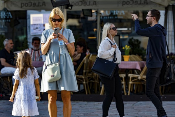 Women on Town Hall Square, Rathausplatz, Rathausplatz, one looking at her cellphone, the other wearing a summer dress, Tallinn, Harju, Estonia