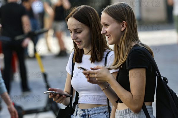 Two young woman laugh together while using their cell phones on the street, Tallinn, Harju, Estonia