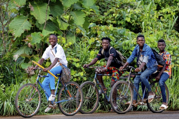 Four young people laugh on bicycles through a green, wooded area, Brobo, Côte d'Ivoire