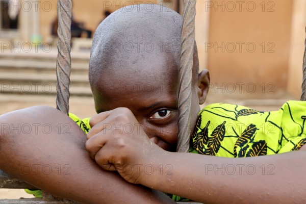 A child looks through metal mesh, a soft smile on his face, Bouké, region, Côte d'Ivoire