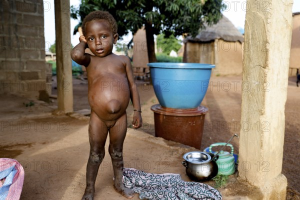 Child standing in front of simple dwellings in a rural village, Nionfouin, zero, Côte d'Ivoire
