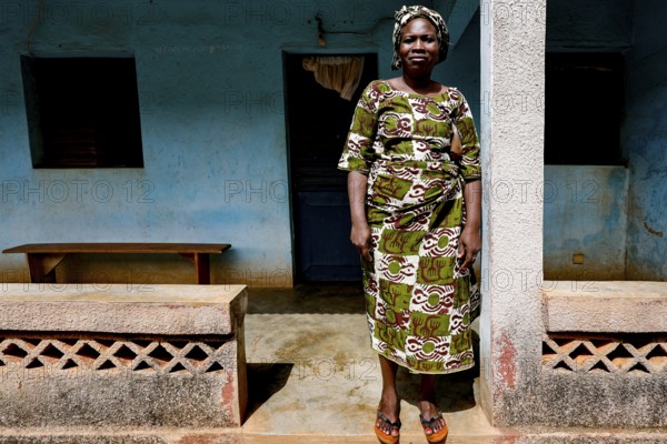 Kinafou stands in front of her house wearing traditional clothes, showing her cultural identity, Korhogo, CI, West Africa