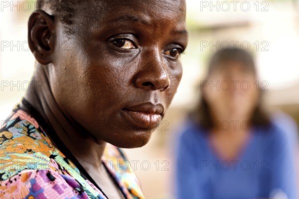 Woman looking thoughtfully during a conversation interview, other person blurred in the background, Korhogo, Côte d'Ivoire