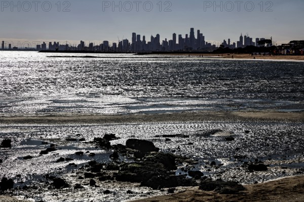 Melbourne skyline seen from Brighton Beach with reflecting sun rays on the water's edge, Brighton Beach, Melbourne, Victoria, Australia