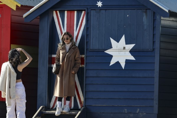Beach visitors in front of a colorful beach house with flag motif in Brighton Beach, Brighton Beach, Victoria, Australia