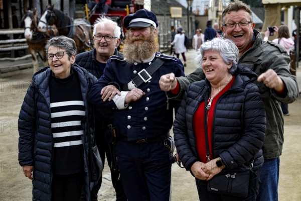 A performer in uniform stands smiling with a group of tourists for photos, Ballarat, Australia
