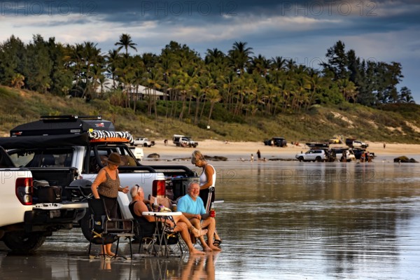 Visitors relax next to cars on Cable Beach car beach, Broome against a palm-covered background, Broome, Western Australia, Australia
