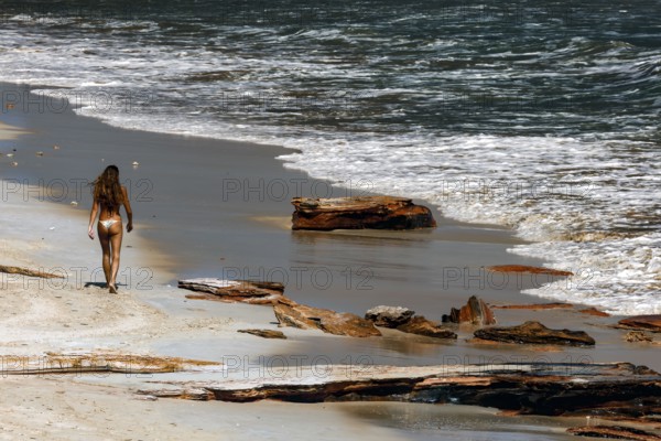 Woman walking along sandy Cable Beach with ocean waves and driftwood in the background, Broome, Western Australia, Australia