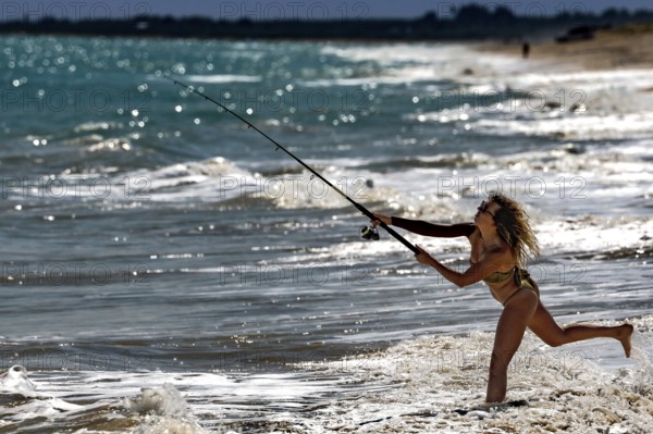 Female fisherman throws her fishing rod into the waves on Cable Beach, Broome, Western Australia, Australia