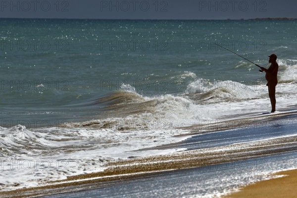 Angler standing on the beach fishing in the waves of Cable Beach, Broome, Broome, Western Australia, Australia