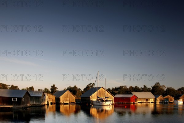 In Käringsund, colorful boathouses are reflected in the water under a clear evening sky, Käringsund, Åland